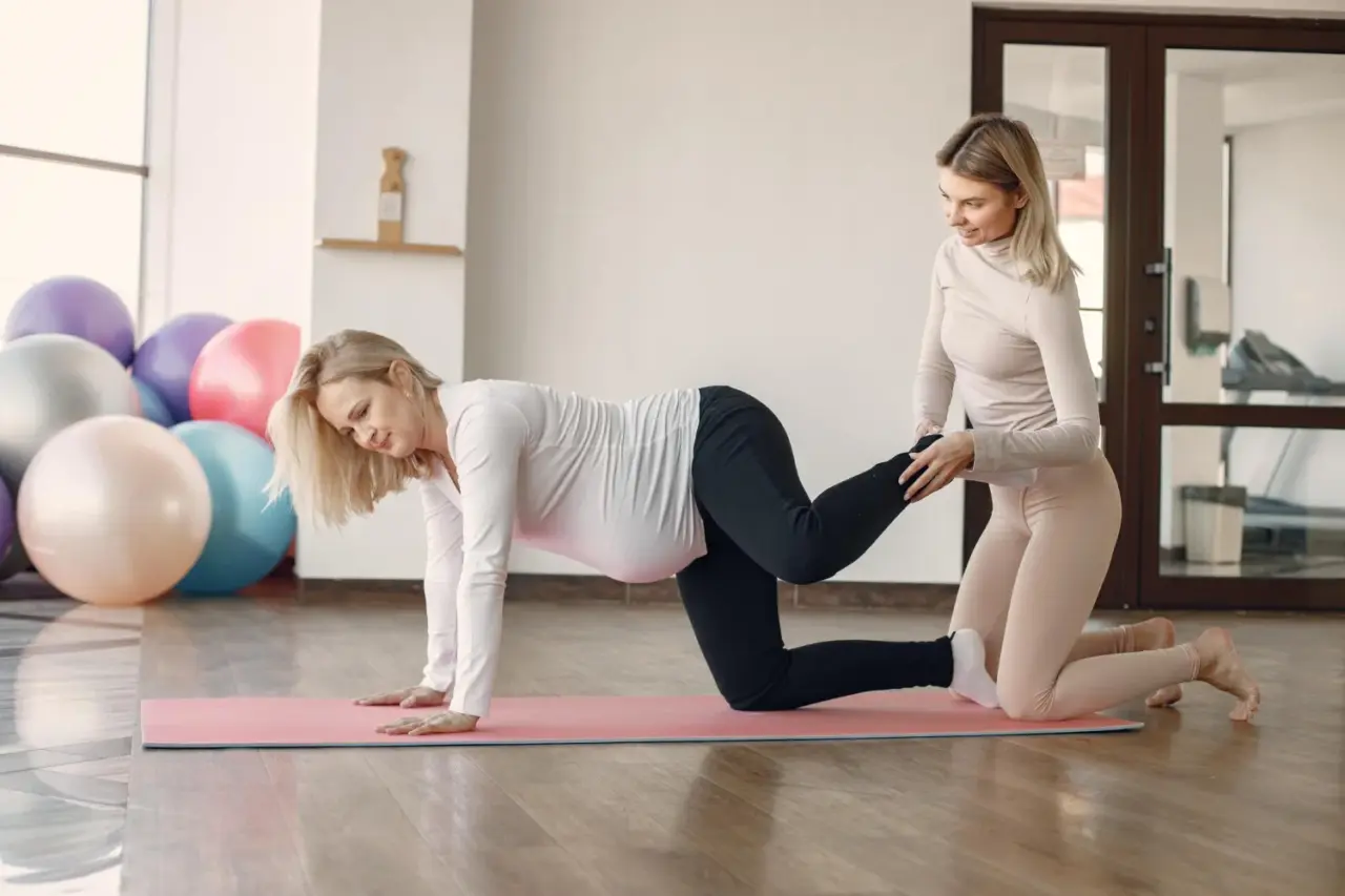 Pelvic floor therapist guiding a pregnant woman through a hands-and-knees exercise on a mat